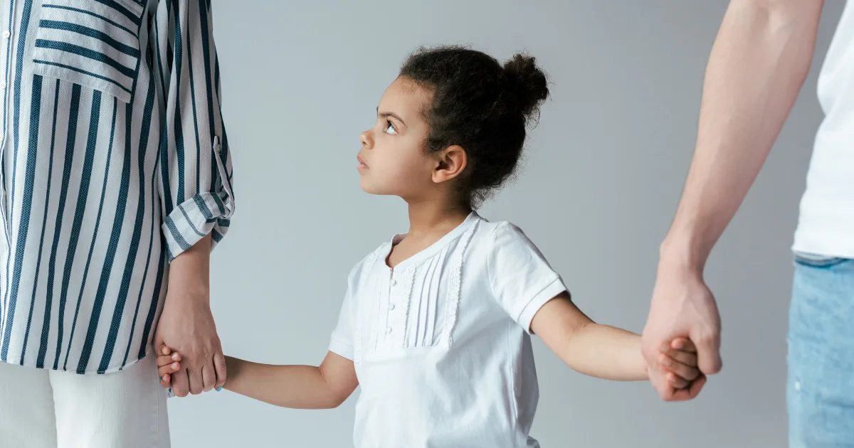 Young girl holding hands with two adults and looking up at one of them