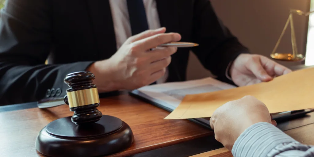 Lawyer at a desk with a gavel handing an envelope of documents to a client