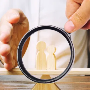Magnifying glass over wooden child figures balanced between red and blue parent figures