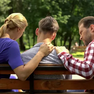 Parents on a park bench comforting a teenage boy seated between them